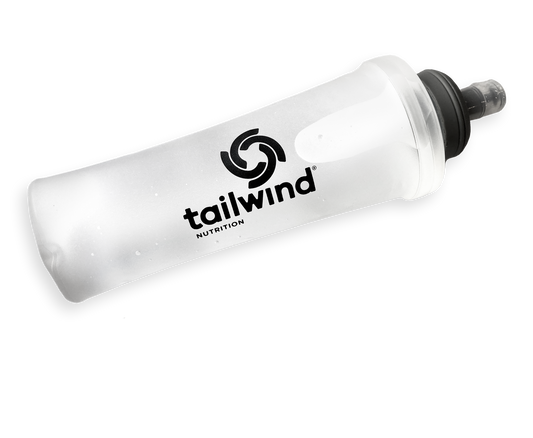 Studio photograph of a Tailwind Nutrition soft flask showcasing a translucent frosted body, a distinctive black swirl logo, and a dark grey bite valve cap set against a solid black background