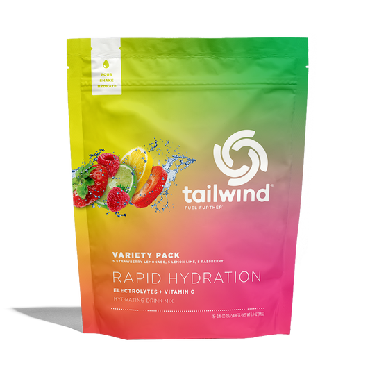 Digital product design for Tailwind Nutrition featuring a Rapid Hydration Variety Pack pouch centered on a white background with its iconic swirl logo, a vibrant green-to-pink gradient, and dynamic splashes of fresh strawberries and citrus fruits