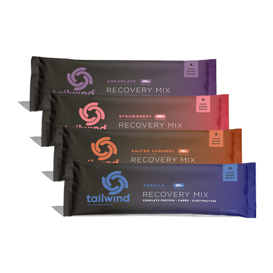Commercial product photography by Tailwind Nutrition showcasing four Recovery Mix sachets stacked diagonally on a white background, featuring the brand's swirling logo, 20g protein badges, and vibrant color-coded packaging in chocolate, strawberry, salted caramel, and vanilla hues