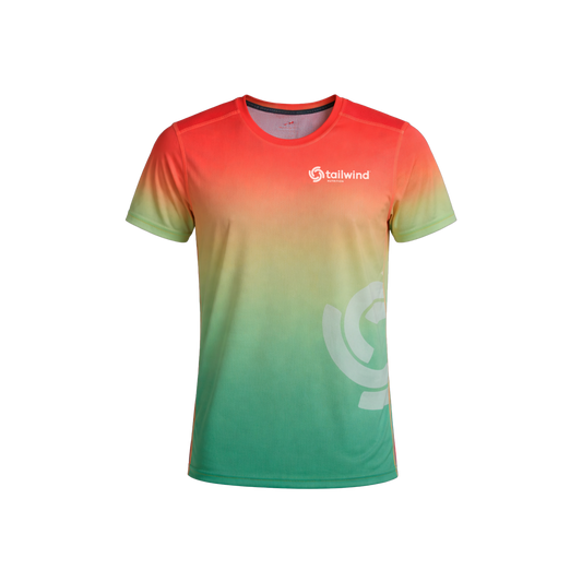 Product photograph of a Tailwind Nutrition athletic t-shirt on a white background featuring a vibrant sunset-inspired gradient from reddish-orange to green with a white chest logo and a large semi-transparent swirl graphic on the side